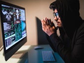 A hooded hacker looking over a hacking tool on monitor of his PC.