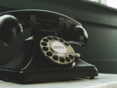 Black rotary telephone on white surface.