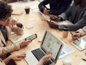 Stock image of business professionals at a table looking at data analytics.