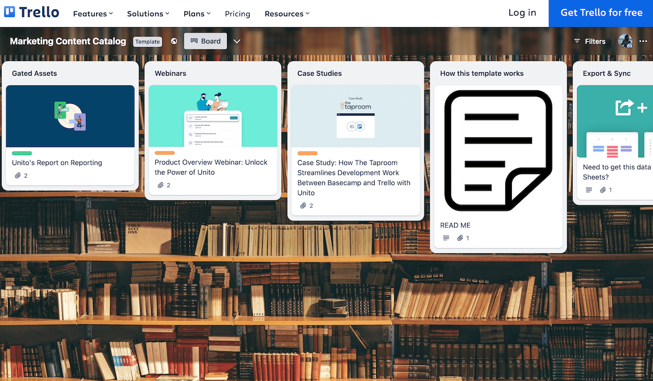 A Kanban board with marketing assets with a wall of books as the background. 