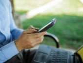 Person sitting with a laptop on their lap and using their mobile device.