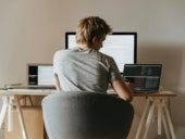 Person sitting at their desk with a laptop and two monitors.