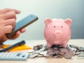 A man using his smartphone app to save money with piggy bank, coins, calculator, paper and pen.