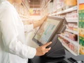 Cropped shot of female cashier staff standing and working with POS or point of sale machine at counter in supermarket.