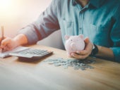 A guy writing down his savings on a paper as he computes the money he saved from a piggy bank.