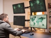 Man sitting in front of multiple large monitors.
