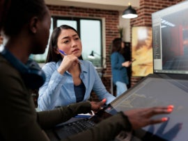 Multiethnic creative game creators sitting at desk with multiple displays while working with 3D assets.