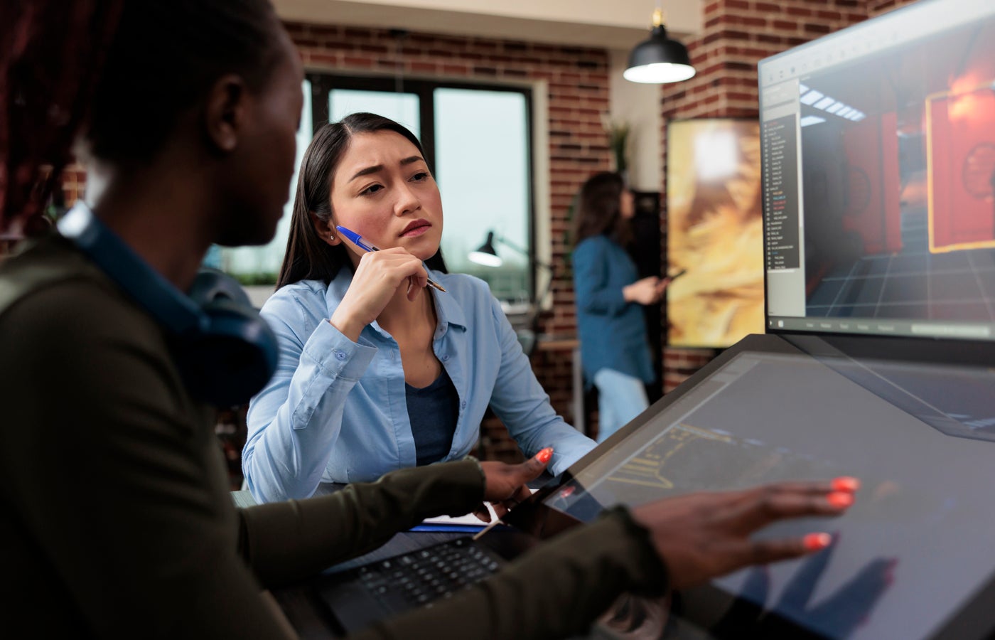 Multiethnic creative game creators sitting at desk with multiple displays while working with 3D assets.