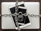 Computer, tablet, phone bound by metal chain and closed with combination lock on wooden table.