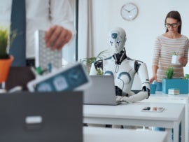Dismissed business people packing their belongings and leaving the office, while a robot is sitting at the desk and working.