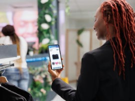 Young customer buying clothes on online boutique app, looking at trendy clothing line on mobile phone website. Female buyer choosing fashion items on e commerce application in shop.
