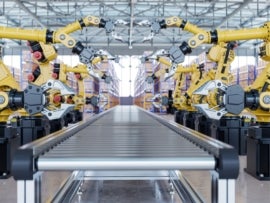 Automated robotic arms with grippers aligned on both sides of a conveyor belt inside a modern industrial warehouse.