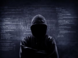 A hooded and unknown hacker with several written codes in the background.