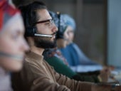 Row of people in headphones looking at computer monitors they working in call center