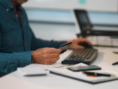 Office worker holding credit card while typing on keyboard, making online payment.