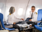 Mature male and female pilots meet inside an airplane, holding hands. Their gesture signifies