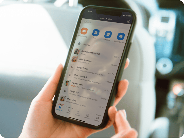 Hand holding a cell phone featuring the Zoom mobile app with message history and meeting options.