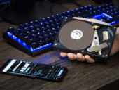 HDD disk in a man's hand against the background of a personal computer and a lying mobile phone next