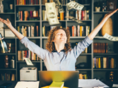 Woman happily throwing cash while sitting inside home office.