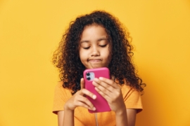 A young girl using a smartphone on orange background.