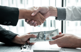 Two business people shaking hands while exchanging cash, symbolizing rapid approval and quick disbursement of business loans for urgent funding needs.