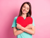 Photo portrait of relaxed woman hugging big red heart card with closed eyes isolated on pastel pink colored background