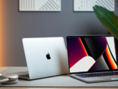 Two Apple laptops sitting on a table next to a plant.