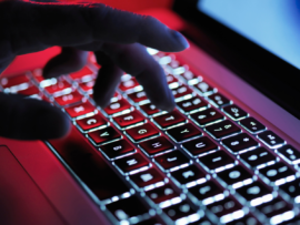 Hand typing on a red backlit laptop keyboard in a dark room