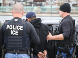 Law enforcement personnel, specifically U.S. Immigration and Customs Enforcement (ICE) agents, detaining a man in handcuffs.