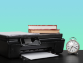 An older black home printer with printed documents and a stack of books, representing legacy hardware affected by Windows 11's 2026 driver update plan.