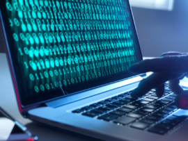 Hands typing on a laptop in a dark room with green binary code displayed on the screen.