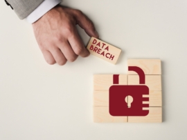 Partial view of man holding brick with 'data breach' lettering over wooden blocks with lock icon.