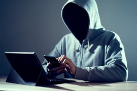 An unknown hooded person hacking a smartphone.
