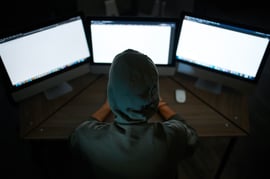 Rear view of an unknown hooded person working on a computer with three monitors.