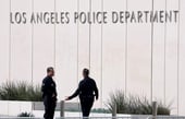 Two Los Angeles Police Department (LAPD) officers standing in front of the department's headquarters building signage.