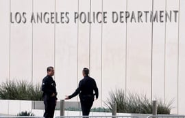 Two Los Angeles Police Department (LAPD) officers standing in front of the department's headquarters building signage.