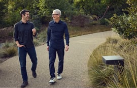 Apple CEO Tim Cook and John Ternus walking and talking on a gravel path at Apple Park.