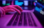 Hands typing on a laptop under purple neon lights